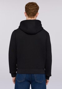 Černá mikina s kapucí na stahovací šňůrku, manžetami a lemem s žebrováním, a měkkou texturou. Zadní strana má jednoduchý, čistý design bez ozdob.