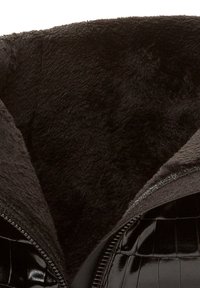 Zbliżenie czarnego futra syntetycznego wewnątrz błyszczącej czarnej kurtki z zamkiem błyskawicznym w wzór krokodylej skóry.