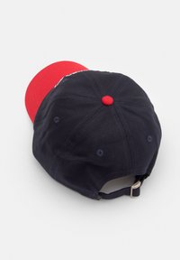 Dunkelblaues Baumwoll-Baseballcap mit einem roten Schirm, das mit Nähedetails und einem roten Knopf oben versehen ist. Verstellbarer Riemen auf der Rückseite.