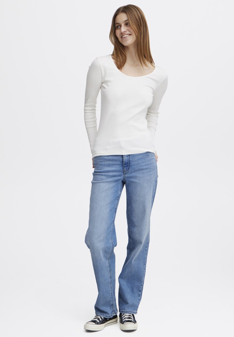 Hvitt langermet topp med rund hals, sammen med lyse straight-leg jeans og svarte kanvas sko. Enkel, uformell design.