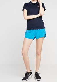 Marinblå polo med krage och korta ärmar, ihopparad med blåa träningsshorts. Svarta sneakers med vit sula. Minimalistisk design.