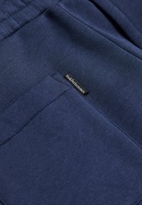 Mørkeblå sweatpants lavet af blødt, tekstureret stof med et synligt logo-tag, der har en elastisk talje og sidelommer.