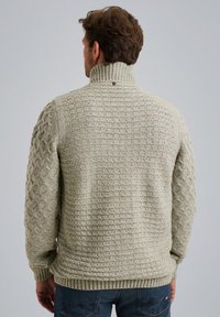 Maglione lavorato a maglia in grigio chiaro con colletto alto. Presenta motivi testurizzati sulla schiena e sulle maniche, polsini e orlo a costine. Nessun logo visibile.