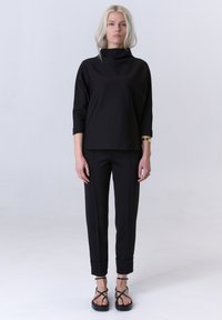 Zwarte driekwart mouw top met een hoge halslijn, gecombineerd met op maat gemaakte zwarte broek met opgerolde manchetten en elegante zwarte sandalen.
