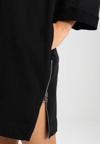 Černé oversized tričko šaty s detaily na zip na levé straně, měkká tkanina a široké krátké rukávy.