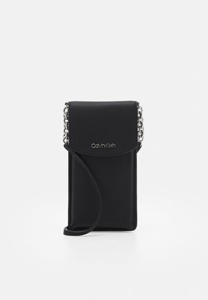 Kleine zwarte leren crossbodytas met klep, zilveren kettingriem en Calvin Klein-logo op de voorste klep.