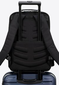 Sac à dos noir avec des bretelles rembourrées et une texture lisse, attaché à une valise à roulettes bleue élégante avec une surface striée.
