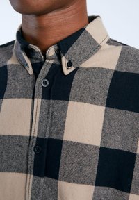 Camisa de franela a cuadros de búfalo en beige y azul marino con cuello tipo button-down, botones negros y textura suave. Patrón a cuadros notable en toda la prenda.
