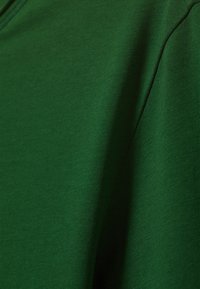 Grüner Baumwollstoff mit glatter Textur, der eine Nahaufnahme von Nähten und Konturen zeigt und die Farbintensität hervorhebt.