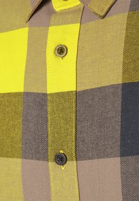 Gele en bruine geruite stof van een overhemd met knoopdetail, met een gestructureerde weving en contrasterende kleuren in rechthoekige patronen.