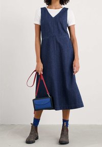 Denim midi šaty s výstřihem do V, bez rukávů a s přiléhavým pasem. Doplněno modro-černou kabelkou přes rameno a hnědými kotníkovými botami.