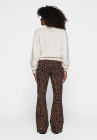 Suéter crema con mangas abullonadas, combinado con pantalones marrones acampanados que presentan un patrón de leopardo negro. Textura suave, acentos mínimos.