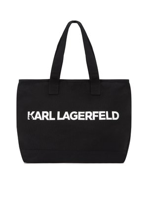 Černá taška přes rameno s dvěma rukojeťmi, s nápisem "KARL LAGERFELD" tučnými bílými písmeny uprostřed přední strany.