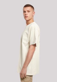 Cream-colored cotton t-shirt with short sleeves and a relaxed fit, featuring a crew neckline and subtle stitching details.