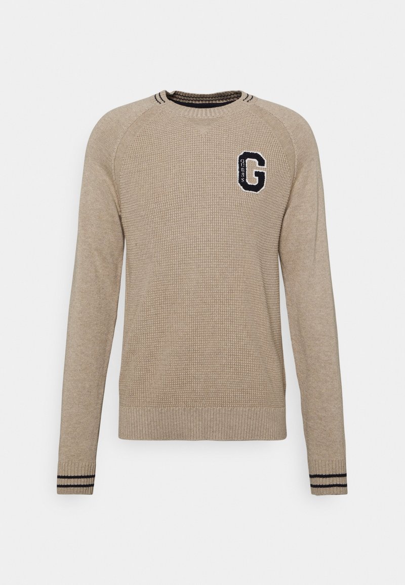 Pull beige en maille à manches longues avec col rond, poignets côtelés rayés noirs, et un écusson noir "G" sur la poitrine gauche.