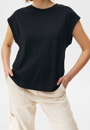 Black short-sleeve t-shirt with a round neckline, made of soft fabric. Paired with light beige utility pants featuring side pockets.