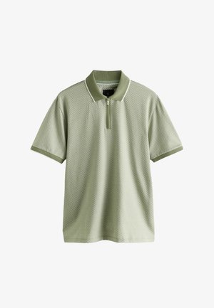Polo de color verde claro con cuello con cremallera, que presenta un patrón texturizado y ribetes en contraste en las mangas y el cuello. Mangas cortas.