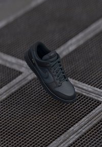 Crne kožne Nike tenisice s okruglim vrhom, perforiranim prednjim dijelom i teksturiranom gumom potplatom. Uključuju vezice i suptilno brendiranje.