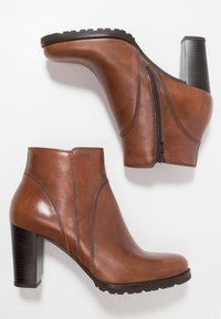 Botas de cuero marrón hasta el tobillo con forma curvada, cremallera lateral y tacón bloque. Suela texturizada para mayor agarre, acabado suave con detalles de costura.