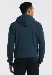 Donkerblauwe hoodie van zacht materiaal, met een grote capuchon, lange mouwen en een ontspannen fit. Geen noemenswaardige patronen of hardware-details zichtbaar.