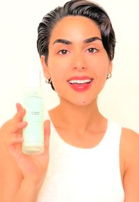 Jasnoniebieska butelka z rozpylaczem i białym pompką, oznaczona etykietą "Scarlett Scented", trzymana przez osobę z krótkimi, ciemnymi włosami, ubraną w białą bluzkę bez rękawów.