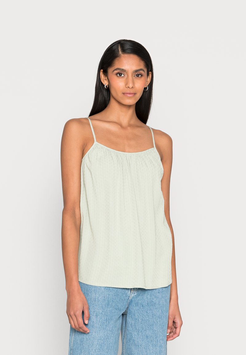 Top sem mangas verde-claro, com alças finas, decote franzido, tecido texturizado e um corte descontraído. Combinado com jeans azul-claro.