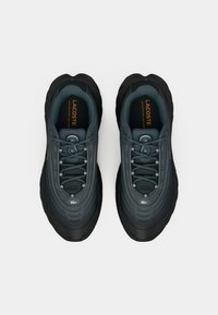 Et par mørkegrå og sorte Lacoste sneakers med snørebånd, runde tåspidser og polstrede indersåler, som viser mærkenavn og logo indeni skoene.