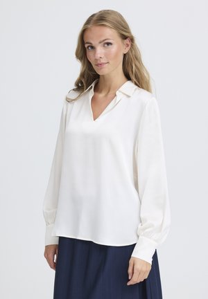 White long-sleeve blouse with a V-neck and buttoned cuffs. Smooth texture and relaxed fit paired with a navy skirt.
