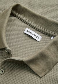 Ελαφρύ πόλο μπλουζάκι σε ελαιί πράσινο με υφή, ριμπ ύφασμα στον γιακά και λευκή ετικέτα της μάρκας Jack & Jones στο εσωτερικό του λαιμού.