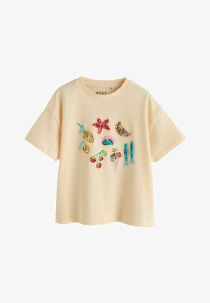 Beige T-shirt met korte mouwen en kleurrijke paillettenapplicaties van fruit, zeesterren, bloemen, ijsjes en vissen aan de voorkant.