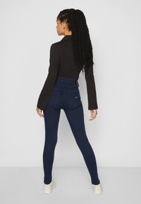Høytlivte, mørkeblå denimjeans med jevn tekstur, med baklommer og et svart belte med firkantet spenne.