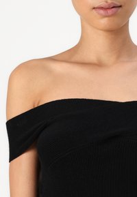 Juodas off-the-shoulder banguotas topas su prigludusiu dizainu, tekstūruotu audiniu ir lygiu apykaklės kraštu. Atskleidžia pečius ir viršutinę krūtinės dalį.