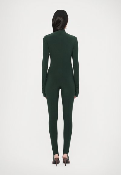 Mono verde de manga larga en diseño ajustado, hecho de material suave, con cuello alto y cobertura de cuerpo completo, combinado con zapatos de tacón alto.
