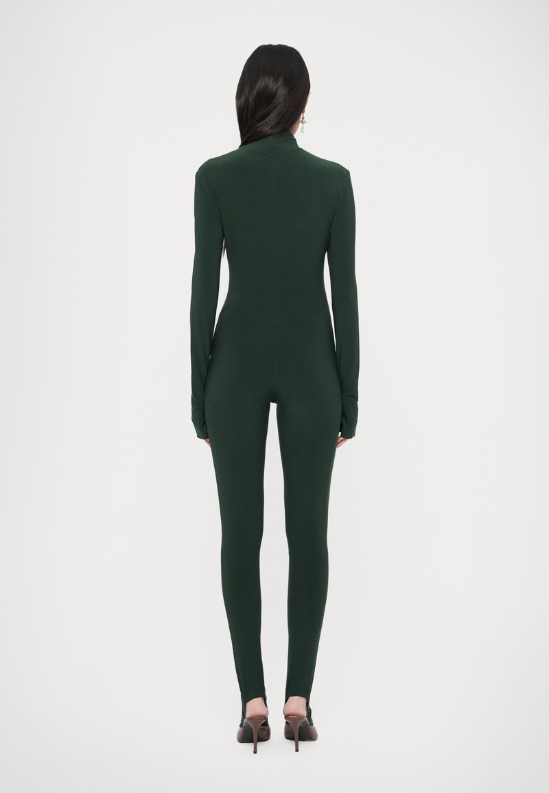 Tuta verde a maniche lunghe dal design aderente, realizzata in materiale morbido, caratterizzata da collo alto e copertura totale del corpo, abbinata a scarpe con tacco alto.