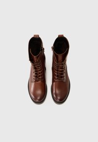 Bottines en cuir marron avec un bout rond, un laçage et une fermeture éclair sur le côté. Texture lisse avec une construction simple et épurée.