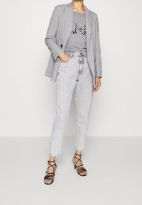 Szara kratkowana marynarka na szarej koszulce z nadrukiem zwierzęcym, w połączeniu z jasnoszarymi jeansami z wysokim stanem i czarnymi sandałkami na cienkich paskach.