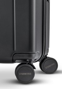 Black travel suitcase with a textured surface, featuring smooth round wheels and a zipper closure. Logo "ETERNITIVE" on the wheels.