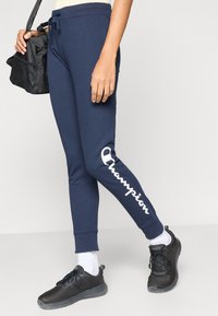 Στενά παντελόνια φόρμας σε ναυτικό μπλε, από βαμβακερό μείγμα με ελαστική μέση και κορδόνι, με λευκό λογότυπο στο αριστερό πόδι.