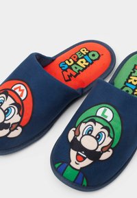 Mörkblå tofflor med plyschmaterial. En har Marios ansikte, den andra Lougis. Klara röda och gröna iläggssulor med texten "Super Mario".