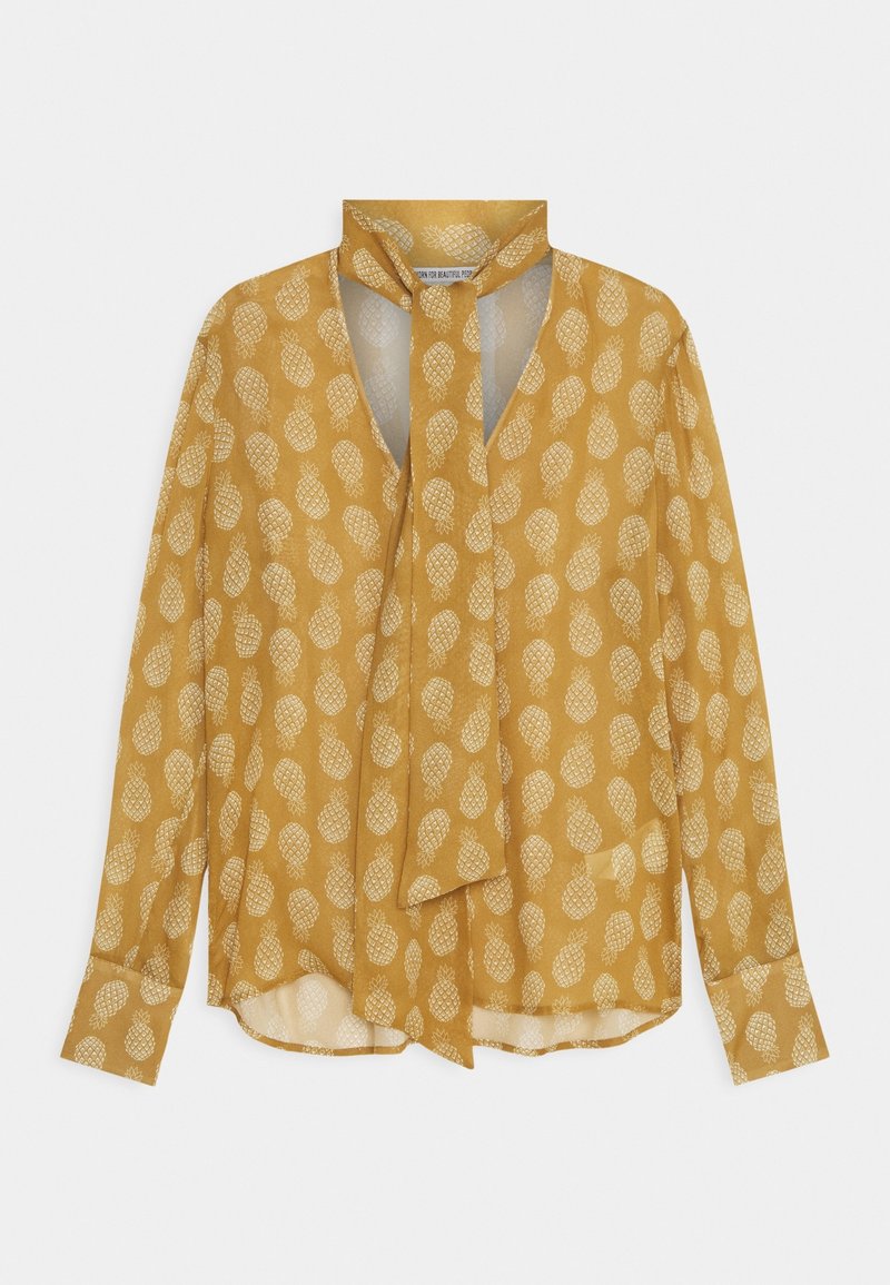 Musztardowo-żółta bluzka na długi rękaw z białym wzorem ananasów i ozdobnym wiązaniem przy szyi.
