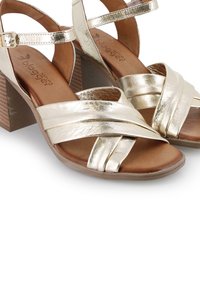 Sandalias de tacón metálicas doradas con tiras cruzadas y un tacón cuadrado texturizado en marrón. Material suave parecido al cuero con plantilla acolchada.