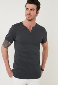 Tricou scurt cu mâneci scurte, de culoare gri închis, cu decolteu în v și trei nasturi maro la guler. Textură netedă, design ajustat și detalii simple de broderie.