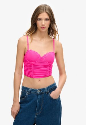 Top corto di un vivace rosa con rifiniture in pizzo, design arricciato e spalline sottili regolabili; abbinato a jeans scuri a vita alta blu.