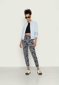 Jaqueta bomber azul claro sobre um top cropped preto, combinada com calças padrão em preto e branco e sandálias brancas com solas pretas.