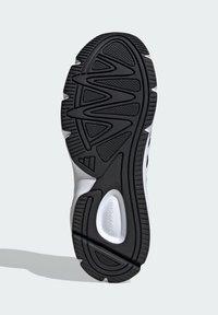 Čierna a biela podrážka športovej obuvi, s textúrovaným gumovým povrchom s ryhami a drážkami na trakciu a s jemne vystúpeným logom.