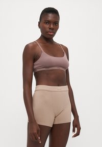 Svijetloružičasti bralette s tankim trakama i UGG logotipom; u kombinaciji s rebrastim bež šortsevima s mekim pojasom i minimalnim šavovima.