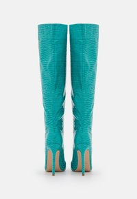 Botas de rodilla en turquesa hechas de material con grabado de cocodrilo. Los finos tacones de aguja y las costuras curvas realzan el diseño ajustado.