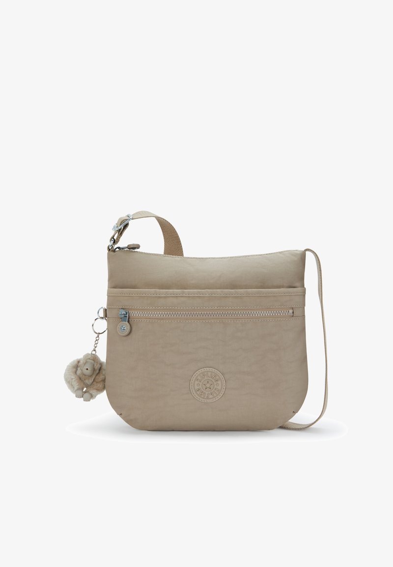 Sac bandoulière beige en tissu texturé, avec une poche zippée à l'avant, un logo circulaire, et un porte-clés singe peluche détachable.