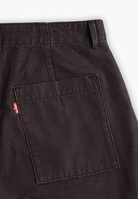 Tamno smeđi platneni hlače s velikim kvadratnim džepom na leđima, s našivenim rubovima i malom crvenom oznakom s natpisom "Levi's".