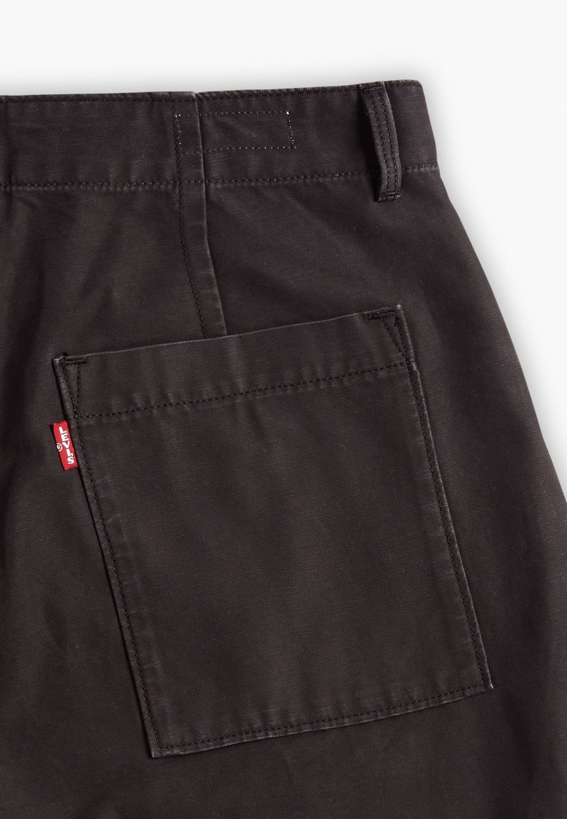 Pantalons en tissu marron foncé avec une grande poche carrée à l'arrière, dotée de bords cousus et d'une petite étiquette rouge avec "Levi's".